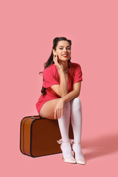 Portrait of beautiful pin-up woman with suitcase on pink background