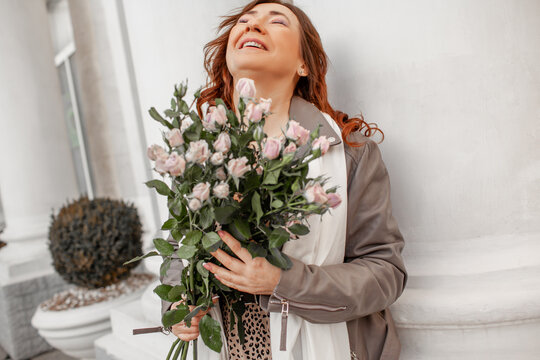 A beautiful middle-aged woman keeps a bouquet of beautiful flowers, purple roses. The girl walks around city and enjoys the cloudy wather