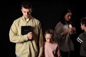 Family with Holy Bible praying together on dark background