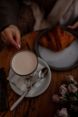 A charmig middle-aged woman drinks latte and eats  croissant in a french cafe on a city street. A woman with flowers is enjoing a wonderful and tasty breakfast