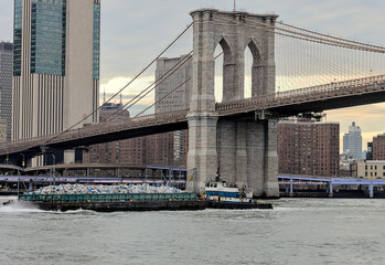 trash barge passing under the brooklyn bridge with downtown manhattan in the background (garbage...