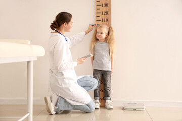 Pediatrician measuring height of cute little girl near wooden stadiometer in clinic - obrazy, fototapety, plakaty