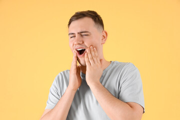 Young man suffering from toothache on color background, closeup