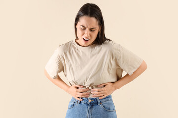 Young woman suffering from bellyache on beige background