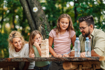 A girl is looking at dices and playing jenga in nature with her family