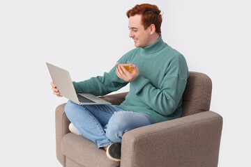 Young man with cup of tea and laptop in armchair on white background