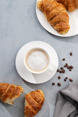 A cup of aromatic cappuccino coffee and fresh croissants on a blue background.