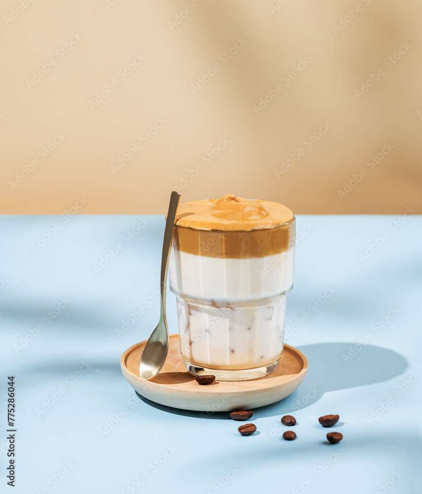 Sticker Vegan dalgona coffee. Whipped instant iced coffee with soy milk in a glass on blue background with coffee bean and shadow.