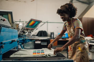 Fotobehang Happy interracial print shop worker putting product into a dryer. © Zamrznuti tonovi