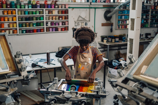 Interracial printing shop worker using squeegee and silkscreen printing