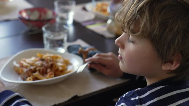 Pensive profile face of a small boy seated at lunch table with contemplative gaze. Child holding fork gazing at the distance while daydreaming about to eat food