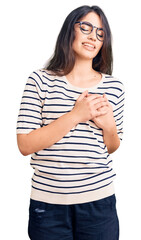 Brunette teenager girl wearing casual clothes and glasses smiling with hands on chest with closed eyes and grateful gesture on face. health concept.