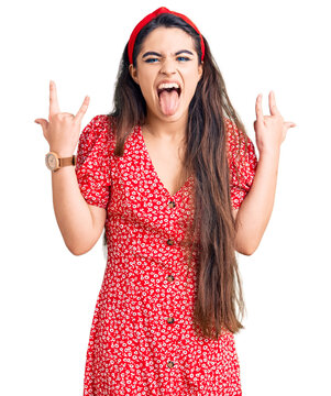 Brunette teenager girl wearing summer dress shouting with crazy expression doing rock symbol with hands up. music star. heavy music concept.