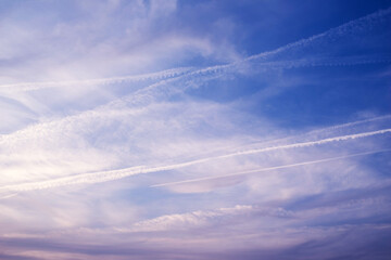 Blue sky background with clouds and white trails from flying airplanes. Roads in the clouds