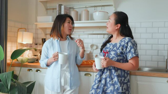 good old friend visit home asian mature woman friend talking standing in kitchen positive conversation good relation friendship reunion home visit casual relax hand hold coffee cup goodvibe at home