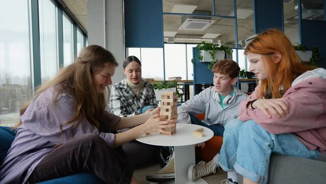 Young happy students spending free time in campus and playing Jenga. Teenagers friends playing a board game made of wooden rectangular blocks