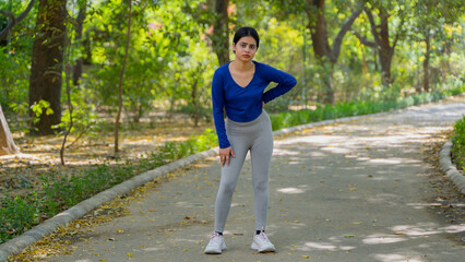 Tired young woman taking rest after doing physical exercise outdoors, fitness concept