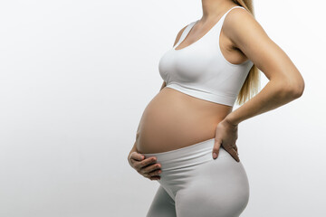 Pregnant woman in white top and leggings suffering from a lower back pain - obrazy, fototapety, plakaty