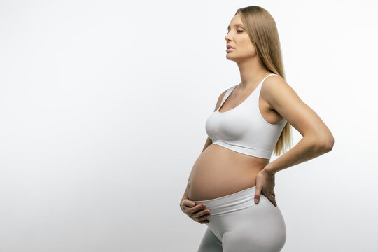 Pregnant woman in white top and leggings holding her hand on her belly
