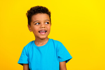 Portrait of cute smart schoolboy with afro hair wear blue t-shirt look at proposition empty space isolated on vivid yellow background