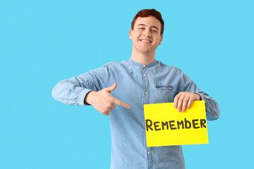 Young man pointing at paper with word REMEMBER on blue background