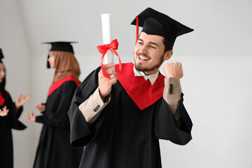 Male graduate student with diploma celebrating success in light room