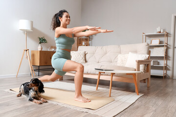 Sporty young African-American woman with cocker spaniel doing yoga at home