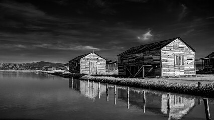 Dramatic black and white image of old wooden weathered storage buildings on a salt processing farm...