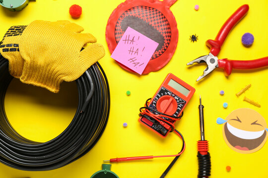 Composition with electrician's supplies and party decor on yellow background. April Fools Day celebration