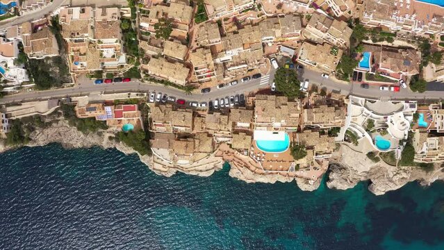 Beautiful aerial flying drone 4K video of Peguera town hotels, houses with tile roofs, swimming pools on rocky Mediterranean waves coastal town with narrow streets. Traveling and vacation concept