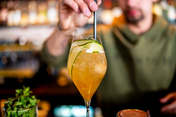 A skilled bartender stirs a refreshing cocktail adorned with a cucumber slice, capturing the...