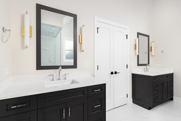 A bathroom with two dark grey cabinets, gold sconces around the mirrors and a marble tile floor. No...