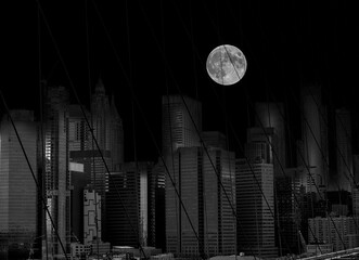    A huge moon above the skyscrapers behind the bars of the Brooklyn Bridge. New. York. Manhattan. black and white night photo with
elements of surrealism.