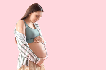 Young pregnant woman with medical patch after vaccination on pink background