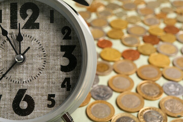 Composition with grey alarm clock and lots of coins on green background. Time management concept....