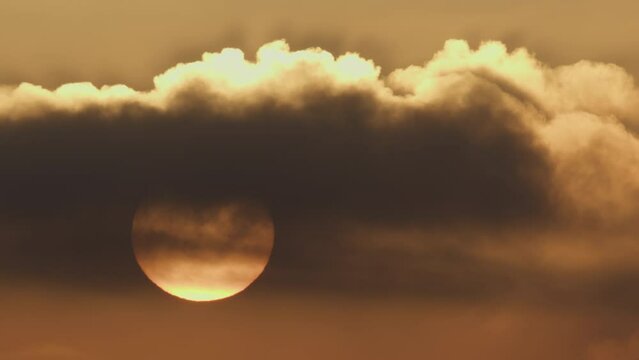 Glowing sun with dark spots visible, partially obscured by clouds at dusk