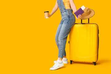 Young woman with suitcase, passport and cup of coffee on yellow background. Travel concept