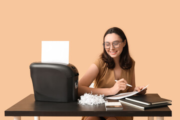 Secretary destroying document in shredder on beige background