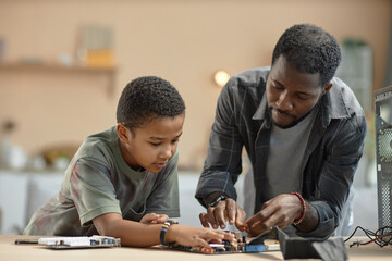 Portrait of African American father and son repairing computer parts together at home, copy space