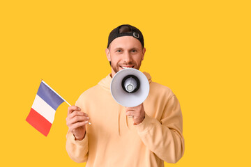 Young man with flag of France and megaphone on yellow background