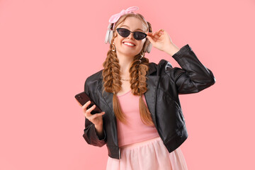 Happy smiling young woman in headphones with braids and mobile phone on pink background
