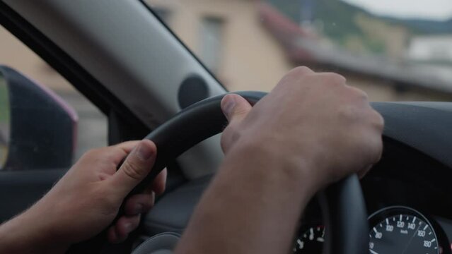 Close-up of a driver's hands firmly gripping the steering wheel of a car, with a partial view of the dashboard and blurred background suggesting movement