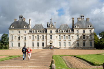 a couple walk towards l'ancien chateau de Cheverny, an historic castle mansion with dark turretted...