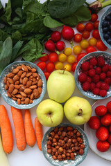 Apples, lemons, bananas, berries, carrots, leek, tomatoes, radishes, spinach and various nuts on white background. Healthy seasonal fruit and vegetable. Top view.