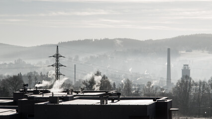 Smoke rises from chimneys against a backdrop of hazy hills, as smog blankets an industrial town at dawn, highlighting environmental concerns. - 775341482