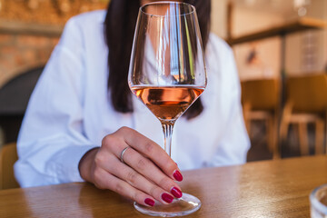 A close up of woman's hand holding a glass with rose wine during the day