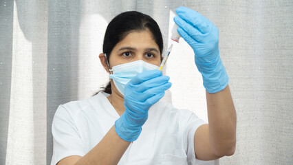 A woman in a white lab coat is wearing blue gloves and a mask