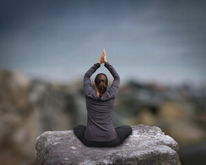 Woman meditating in a yoga position outdoors overlooking serene nature.