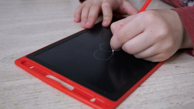 Close-up view of childs hands drawing a flower on a red doodle board.