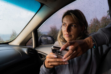 mujer joven latina con su rostro serio dentro de su auto usando su teléfono móvil y con su rostro muy pensativo 